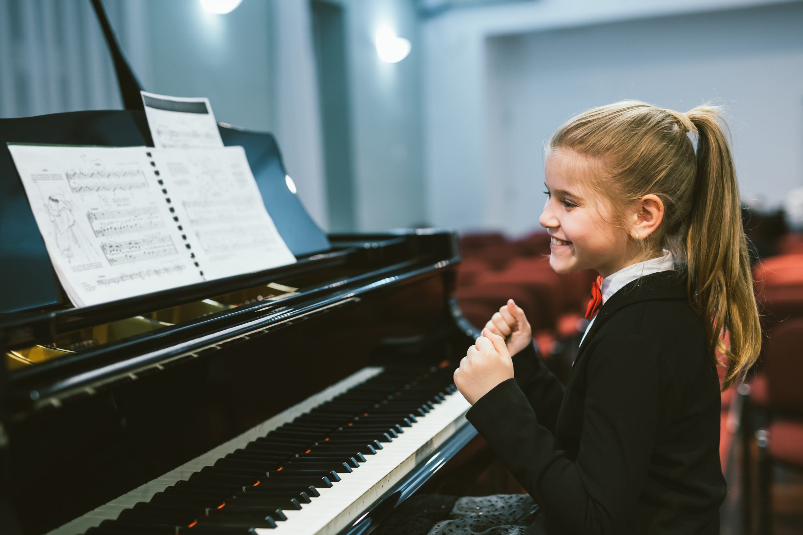 happy little girl teaching to play piano in music school